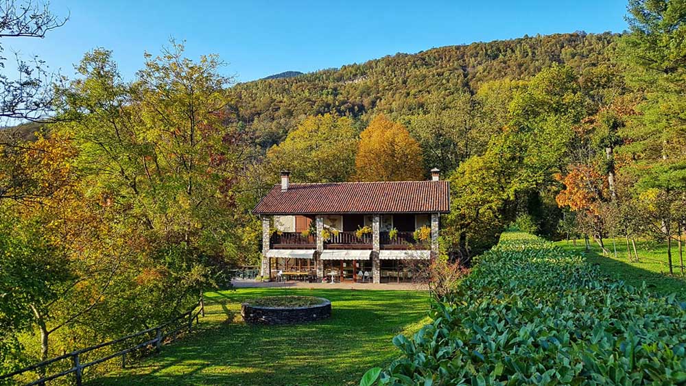 Northern Italy farmhouse surrounded by lawn, trees and hillside